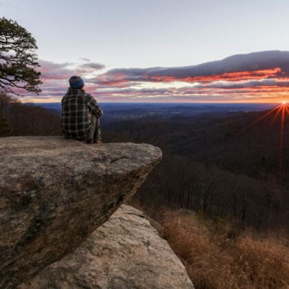man sitting on rock watching sunset